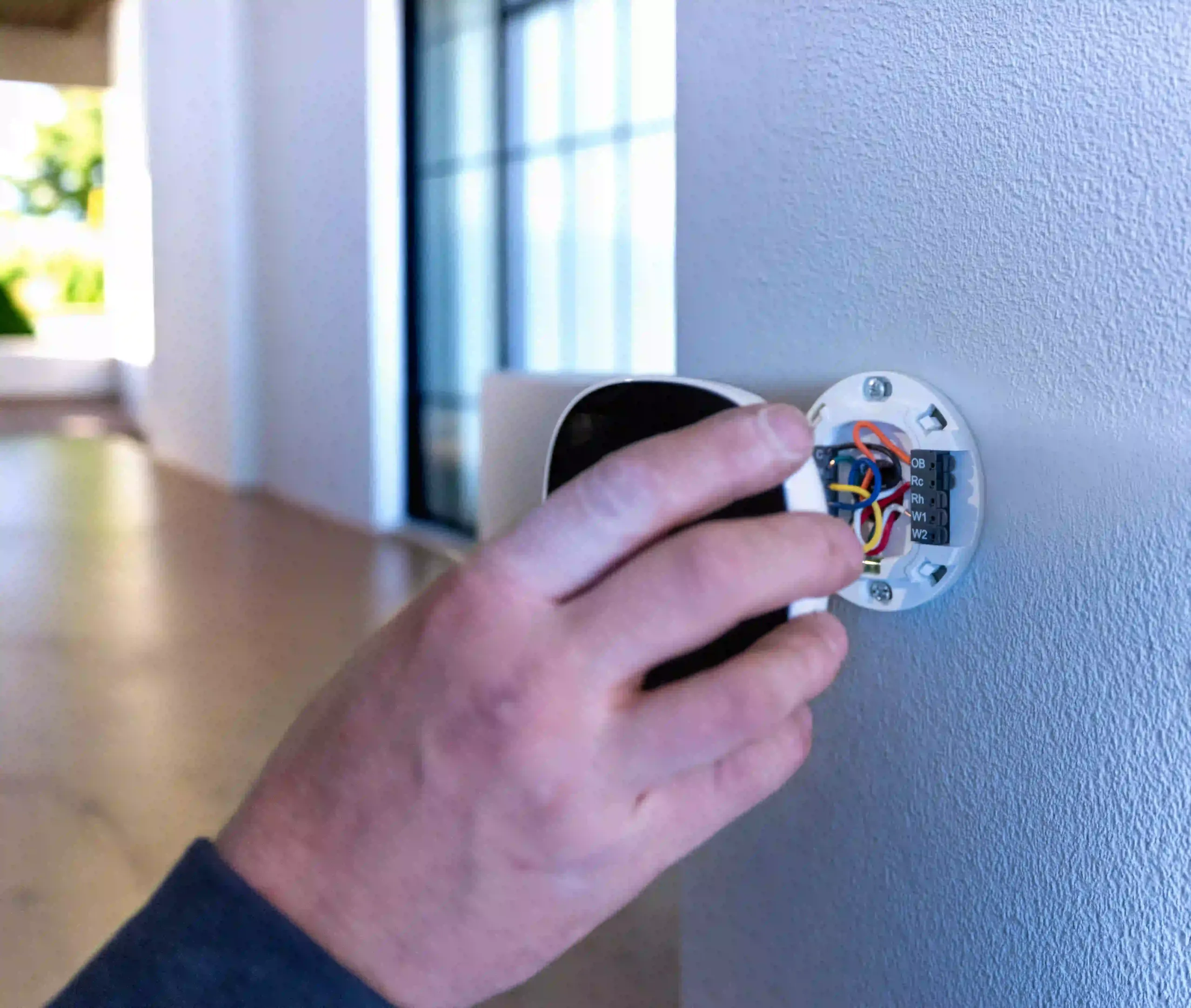 Technicien branchant un thermostat mural pour un système de chauffage et climatisation résidentiel